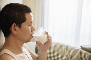 asiatisk man dricker mjölk efter att ha vaknat på morgonen sittande på en säng - hälsovårdskoncept foto