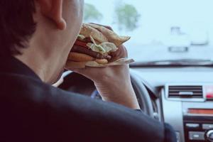 man kör bil medan han äter hamburgare foto