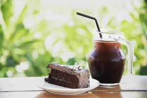 chokladkaka på bordet med iskaffe över grön trädgårdsbakgrund - koppla av med dryck och bageri i naturkoncept foto