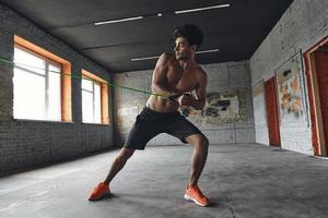 full längd av koncentrerad ung man tränar med elastiskt motståndsband i gymmet foto