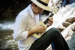 man spelar ukulele ny till vattenfallet - människor och musikinstrument livsstil i naturen koncept foto