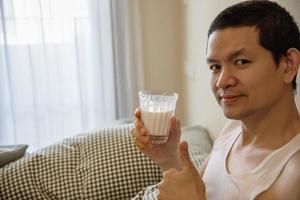 asiatisk man dricker mjölk efter att ha vaknat på morgonen sittande på en säng - hälsovårdskoncept foto