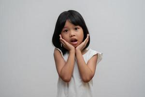 porträtt av asiatiskt barn 5 år gammal och att samla hår och placera händerna på hakan och göra tänkande poserar på isolerad vit bakgrund, hon är lycka, utstrålning i ungdomen, utbildningskoncept foto