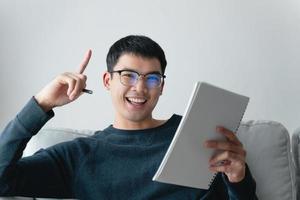 ung omtänksam asiatisk man i glasögon tänker och tittar på anteckningsboken. foto