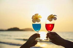 siluett par hand som håller cocktailglas dekoration med plumeria blomma med strand bakgrund - glad slappna av firande semester i havet natur koncept foto