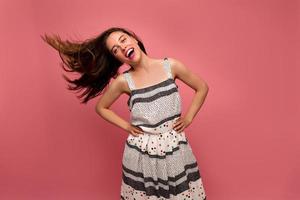 studio skott av glad dansande dam i sommarklänning med flygande hår över rosa bakgrund foto