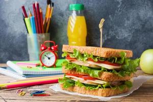 hälsosam lunch till skolan med smörgås, färskt äpple och apelsinjuice. diverse färgglada skolmaterial. kopieringsutrymme. foto