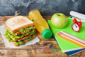 hälsosam lunch till skolan med smörgås, färskt äpple och apelsinjuice. diverse färgglada skolmaterial. kopieringsutrymme. foto