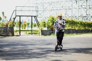 asiatisk man åker elektrisk skoter medan du tittar på telefonen på Park Street. modernt och ekologiskt transportkoncept. foto