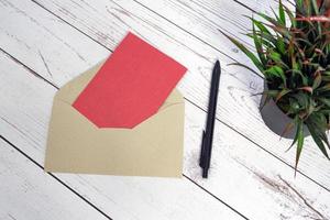 rött kort mockup med kuvert, penna och krukväxt på träbord. foto