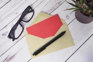 rött kort mockup med kuvert, penna, läsglasögon och krukväxt. kopieringsutrymme foto
