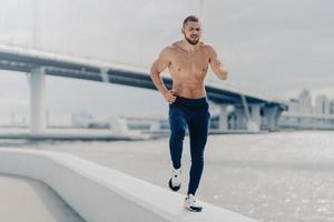 atletisk ung skäggig man går in för sport har morgonlöpning andas djupt förbereder sig för att springa maraton. motiverad idrottsman som joggar vid floden har en stark frisk kropp. fitness och sport koncept foto