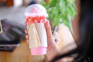 hand som håller en jordgubbssmoothie milkshakemugg insvept i tomt silkespapper, kafé, kopieringsutrymme foto