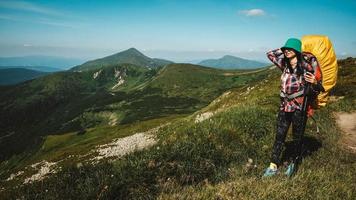 kvinna turist går på en vandringsled med en ryggsäck mot bakgrund av gröna berg och himmel foto