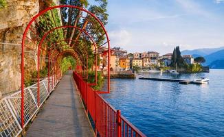 röd trädgårdsbåge på kustlinjen som leder mot den vackra och historiska staden Varenna vid kanten av comosjön i den norra italienska regionen Lombardiet foto