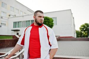 ung brutal skäggig muskulös man bär på vit sport kostym med röd skjorta. foto