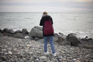 flicka tar bilder av stranden. kvinnlig fotograf. sök efter berättelse för ram. stora stenar. stenig strand. foto