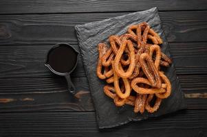 hemlagad churros med choklad på en mörk trä rustik bakgrund. foto