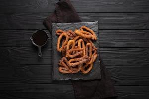 hemlagad churros med choklad på en mörk trä rustik bakgrund. foto