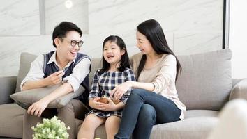 glad asiatisk familj tittar på tv tillsammans och spenderar tid i karantän på soffan i vardagsrummet. familj och hem koncept. foto