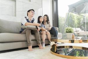 glad asiatisk familj tittar på tv tillsammans och spenderar tid i karantän på soffan i vardagsrummet. familj och hem koncept. foto
