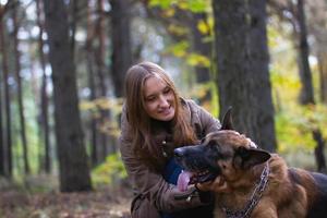 ung söt leende flicka leker med schäferhund utomhus i höstskogen foto