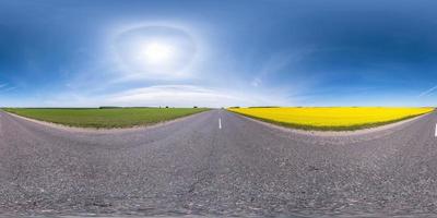 hel sfärisk sömlös panorama 360 graders vinkelvy på trafikfri asfaltväg bland rapsfält med klar himmel med gloria i ekvirektangulär projektion, vr ar innehåll foto