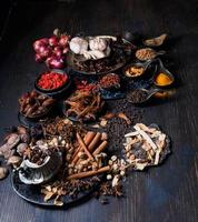 ovanifrån foto massor av vitlök, lök, paprika, chili och torkade örter, placerades på tallrikar och koppar på en svart träbakgrund. delades för att förbereda att laga mat Indien hälsosam mat