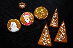 handgjorda festliga pepparkakor i form av stjärnor, snöflingor, människor, strumpor, personal, vantar, julgranar, hjärtan för jul och nyårshelg på svart träbakgrund foto