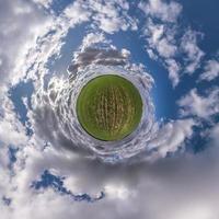 liten planet i blå himmel med sol och vackra moln. transformation av sfäriskt panorama 360 grader. sfärisk abstrakt flygfoto. utrymmets krökning. foto