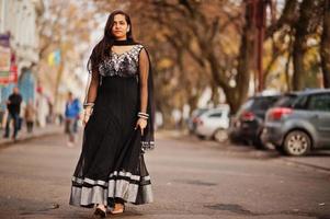 söt indisk flicka i svart saree klänning poserade utomhus på höstgatan. foto