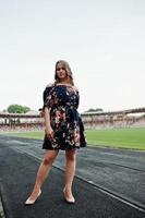 porträtt av en fantastisk tjej i klänning och höga klackar på banan på stadion. foto