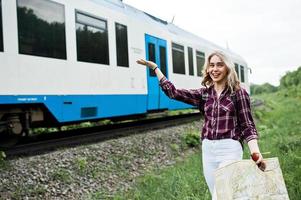 porträtt av en ung blondin i tartanskjorta bredvid tåget med en karta. foto