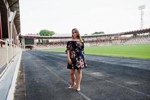 porträtt av en fantastisk tjej i klänning och höga klackar på banan på stadion. foto