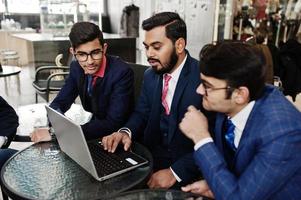 grupp av tre indisk affärsman i kostym sitter på kontoret på café och tittar på laptop. foto