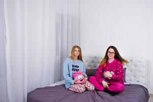 två vänner flickor i pyjamas ha kul på sängen på rummet. foto