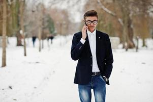 snygg indisk student man i kostym och glasögon poserade på vinterdag utomhus och talar i mobiltelefon. foto