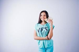 porträtt av en attraktiv tjej i blå eller turkos t-shirt och byxor poserar med mycket pengar i handen. foto