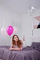 ung flicka med ballonger på sängen poserade på studio rum. foto