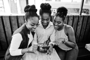 tre afroamerikanska flickor sitter på kaffebordet och tittar på mobiltelefonen. foto