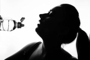 svartvita porträtt av glada attraktiva unga fitness kvinna i topp med flaska vatten isolerad över vit bakgrund. foto