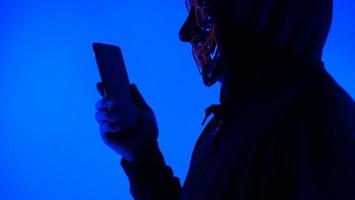 anonym hacker och ansiktsmask med smartphone i handen. foto