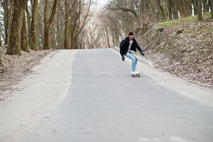 street style arabisk man i glasögon med longboard longboarding på vägen. foto