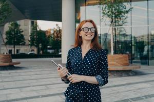 framgångsrik lycklig kvinna entreprenör bär bärbar dator anteckningsbok medan du står på stadsgatan foto