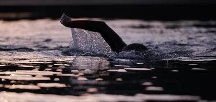 triathlon idrottare simmar på sjön i soluppgången bär våtdräkt foto
