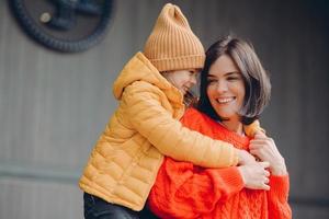 foto av positiv underbar mamma och litet barn omfamnar vänliga, har goda relationer, visar sanningsenliga känslor, bär moderiktiga outfits, le positivt. familj och barn koncept