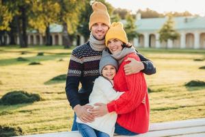 utomhus porträtt av vacker leende kvinna, stilig man och deras lilla söta dotter står tillsammans mot forntida bilduing i parken, bär varna stickade kläder, har intressant utflykt foto