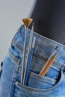 penslar och pennor i fickan på flickans jeans på en grå bakgrund. konstnär målning koncept. foto