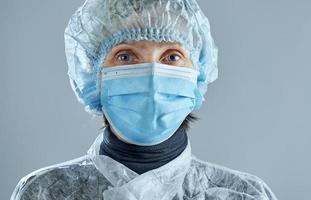 kvinna medicinsk ansiktsmask på en grå bakgrund. foto med kopia utrymme. en kvinna i en medicinsk engångsdräkt.