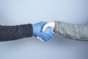 skakar hand i medicinska handskar på en grå bakgrund. konceptet med ett säkert handslag. foto